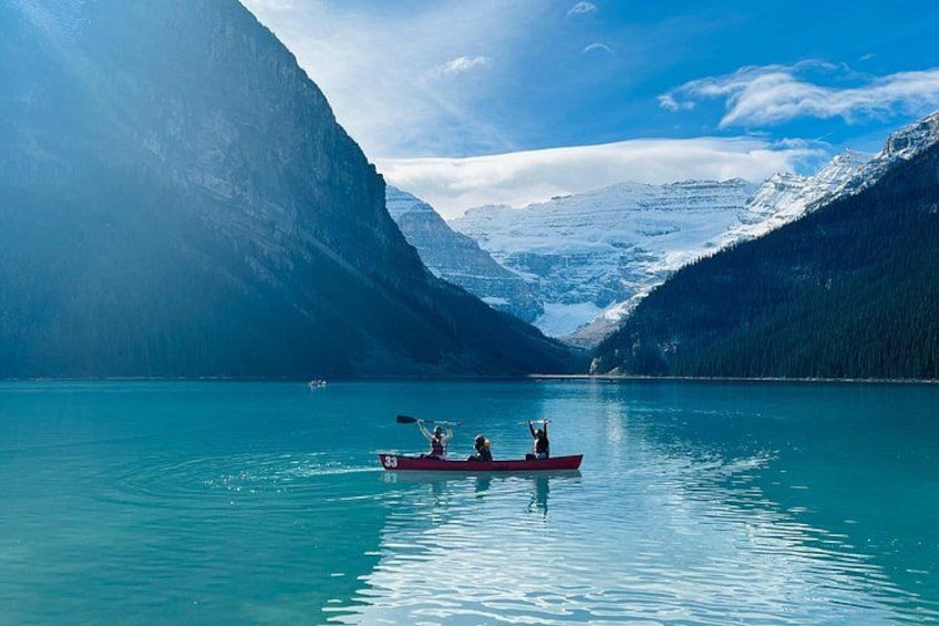 A calm lake with a red canoe, two people paddling, surrounded by snow-capped mountains. 2