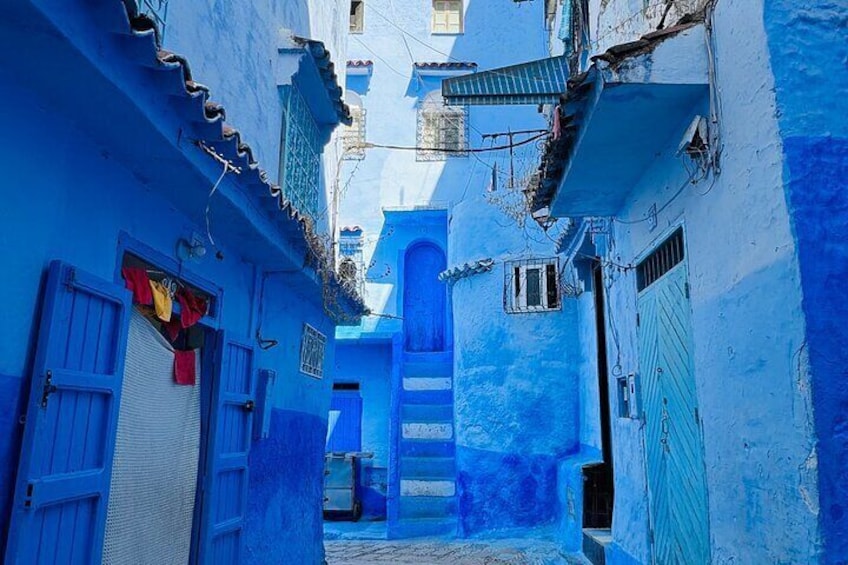 A narrow alleyway with blue-painted buildings, a staircase, and a small window. 5