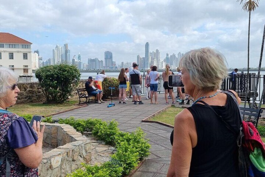 En havnefront med mennesker, der går og sidder, med udsigt over byens skyline. 3