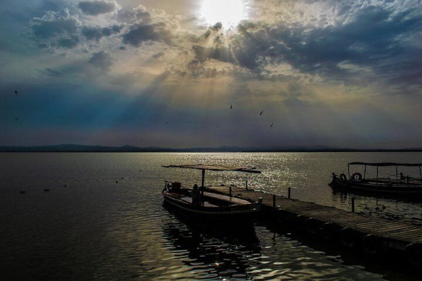 A calm lake with boats docked at the pier, a clear sky, and a distant horizon. 4