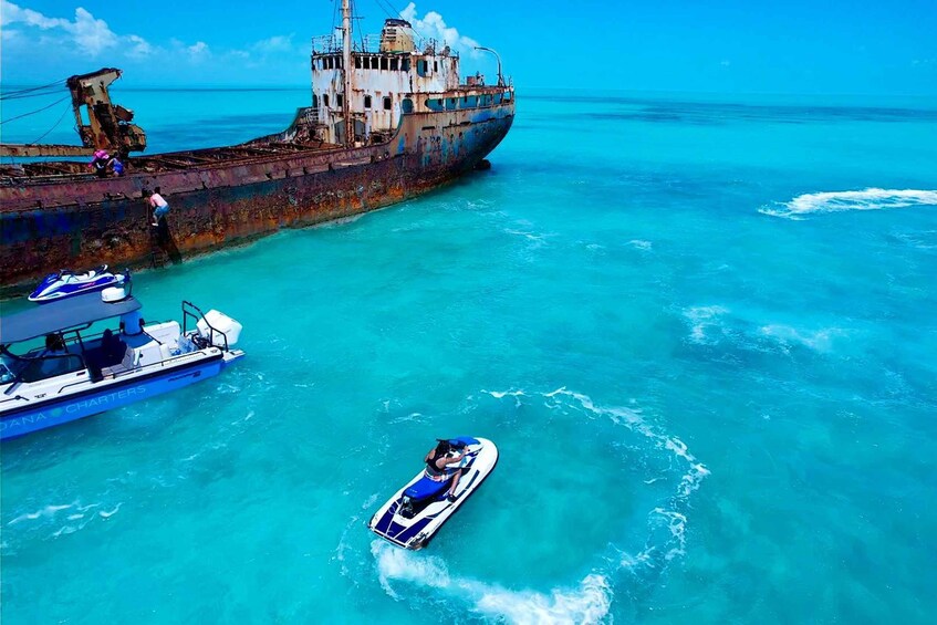 A large rusted shipwreck in clear turquoise waters with a jet ski and a small boat nearby. 5