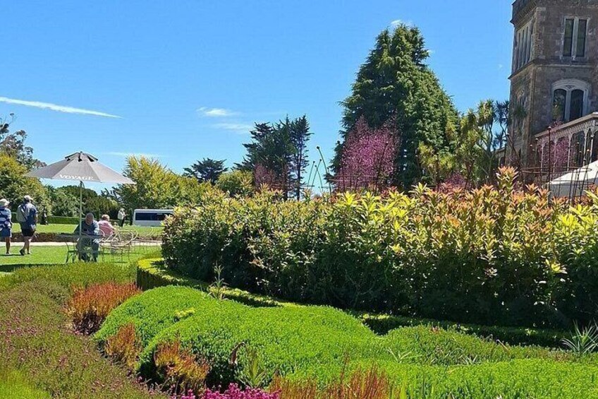 A well-manicured garden with hedges, a variety of flowering plants, and a large building in the background. 2