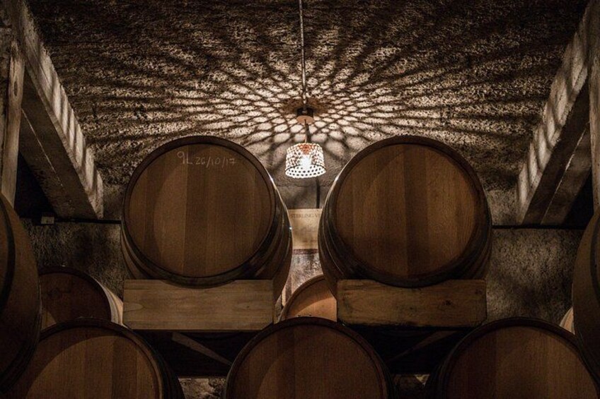 Wooden wine barrels in a cellar with a hanging light fixture. 2