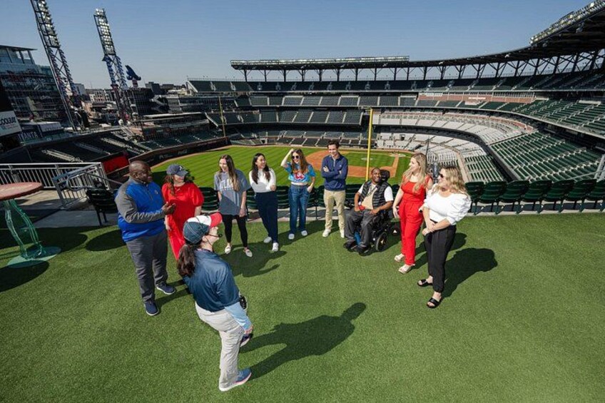 A group of people standing on a baseball field with a stadium in the background. 2