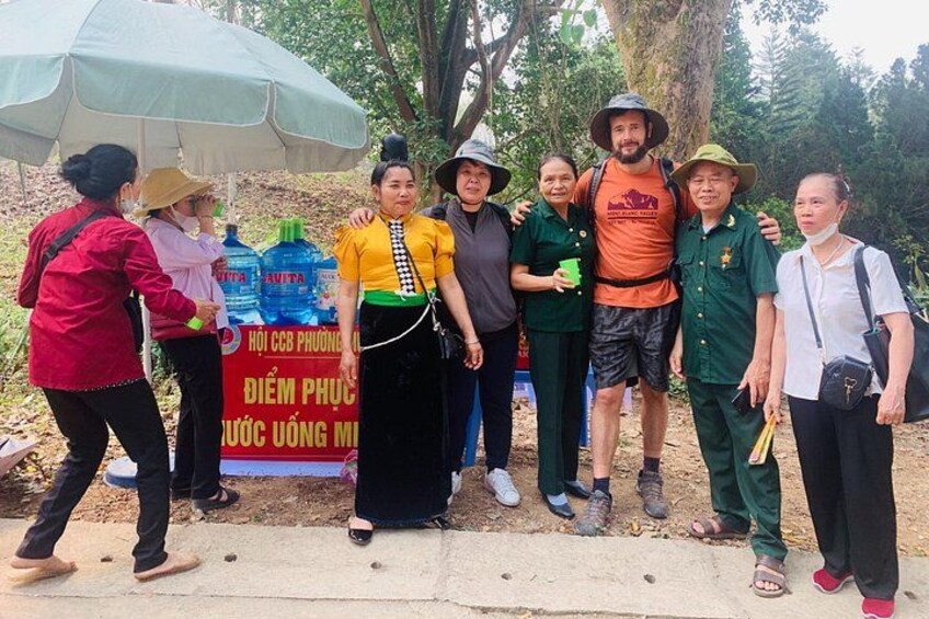 A group of people standing in a natural setting with trees and a banner in the background. 4