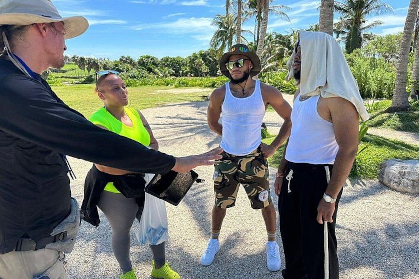 A group of people outdoors, one holding a clipboard, in a tropical setting with palm trees and a clear sky. 5