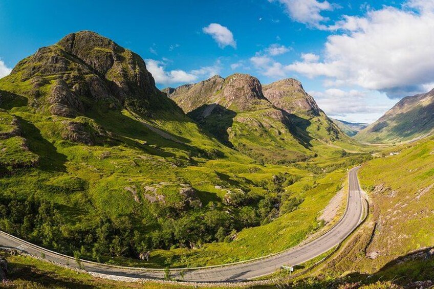 Una carretera sinuosa que serpentea por un valle verde y exuberante, con afloramientos rocosos y un cielo azul despejado. 3