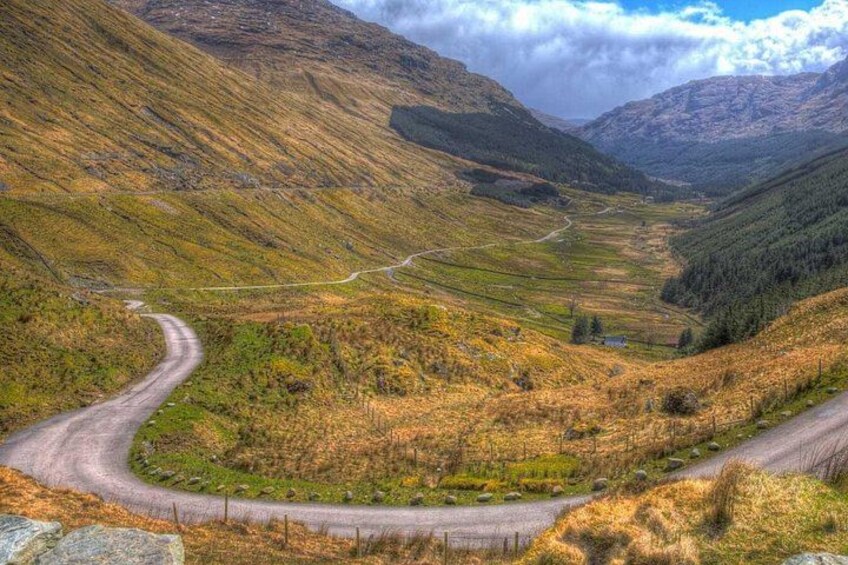 A winding road through a valley with grassy terrain and distant mountains. 4