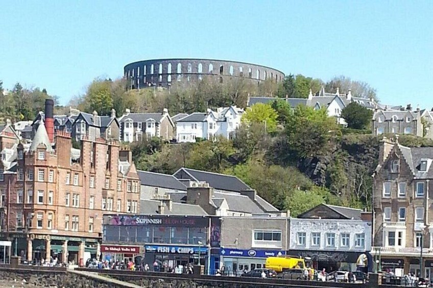 A coastal town with historic buildings, a prominent round tower, and a busy waterfront with shops and people. 2