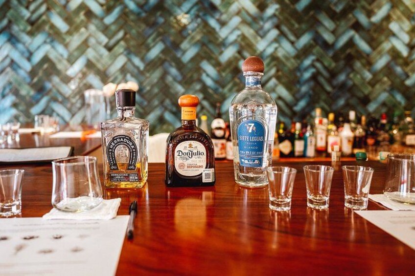 Bar con botellas de Don Julio y otras licores, vasos y un muro tejido al fondo. 3
