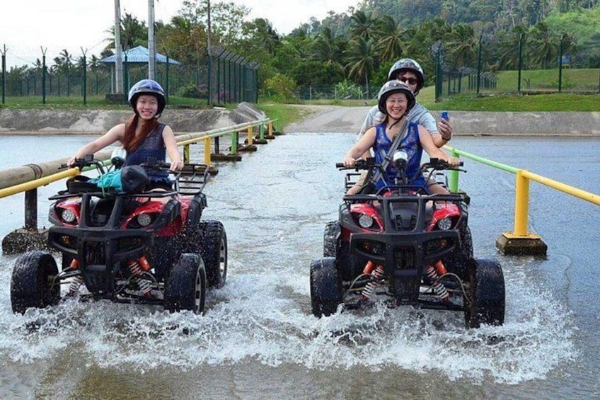 Two people riding ATVs on a water trail surrounded by greenery. 1