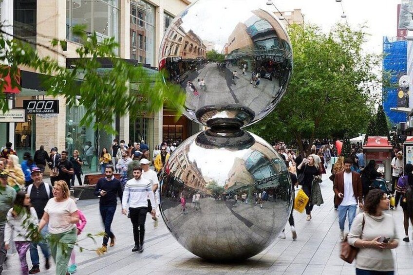 A large metallic sculpture in a busy urban setting with pedestrians. 1
