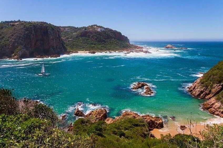 Paisaje costero con aguas turquesas cristalinas, afloramientos rocosos y un velero. 5