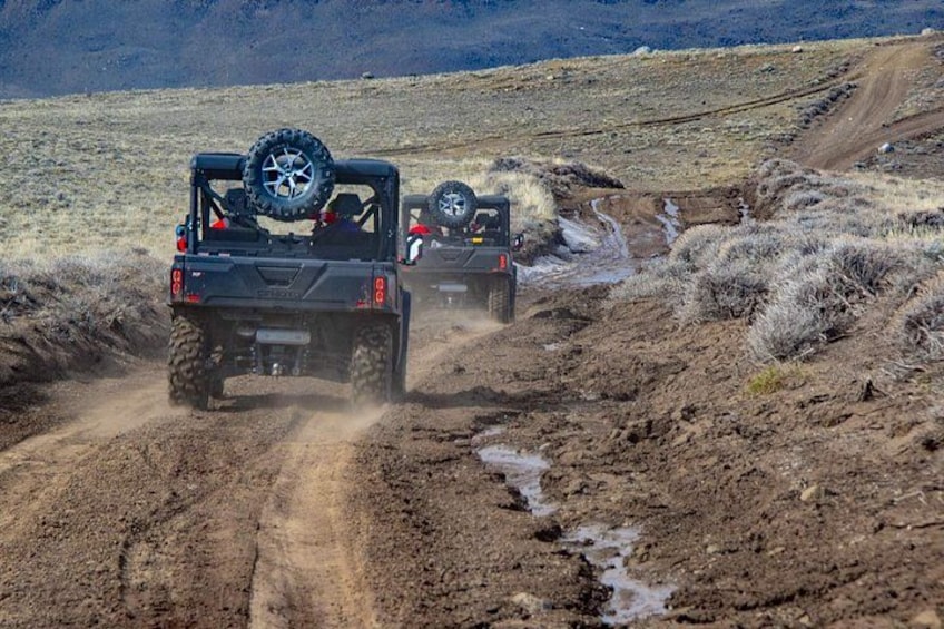 Zwei Geländewagen auf einem schlammigen Pfad in einer trockenen, offenen Landschaft. 5