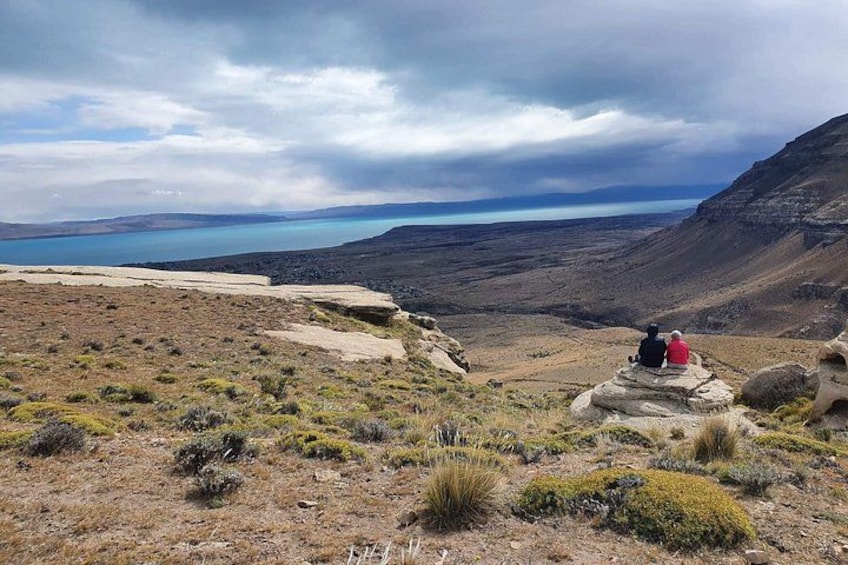 Eine Berglandschaft mit einem See und zwei Personen, die auf einer Felsformation sitzen. 3