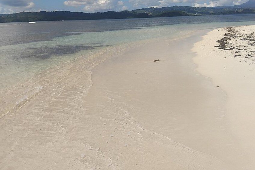 Een zandstrand met helder water en bergen in de verte. 1