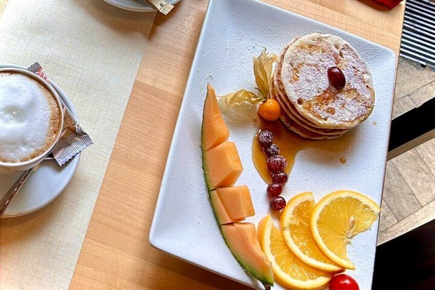 A breakfast plate with pancakes, orange slices, and a cup of coffee. 2