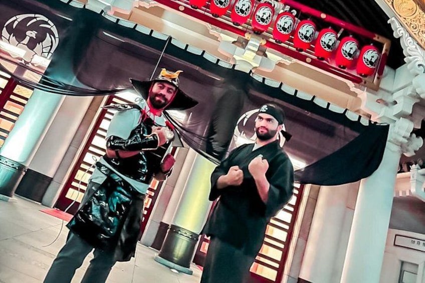 Two individuals in a theatrical setting with a stage backdrop and architectural columns. 3