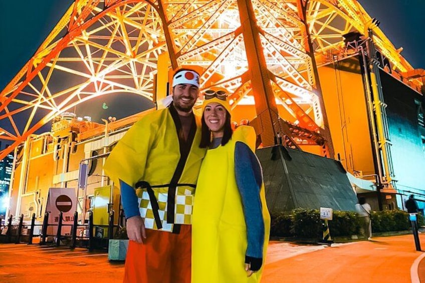 A person in a yellow raincoat and a person in a yellow and blue raincoat standing in front of a large, illuminated Ferris wheel. 3