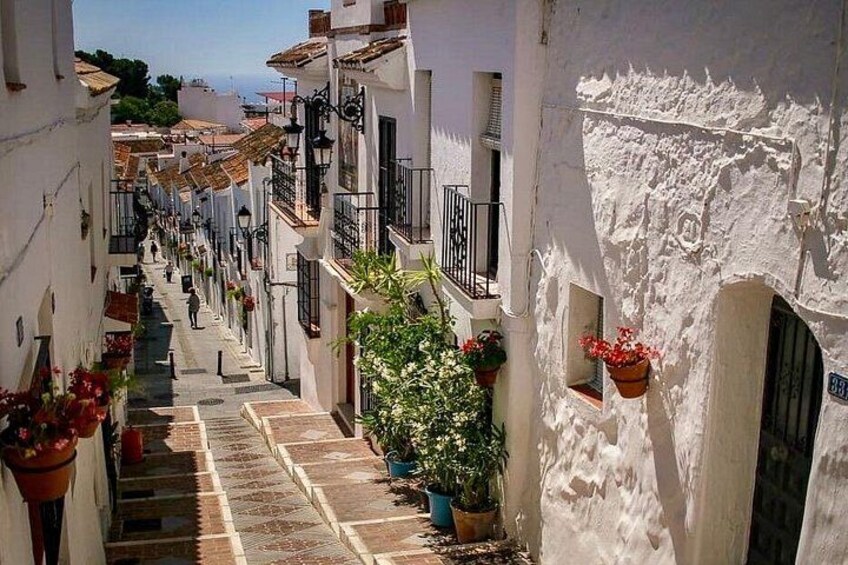 A narrow street with white buildings, potted plants, and a staircase leading up. 5