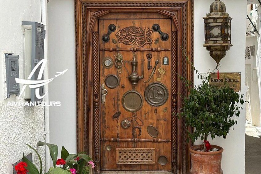 Une porte en bois ornée de motifs métalliques complexes, une plante en pot et une lanterne fixée au mur. 5