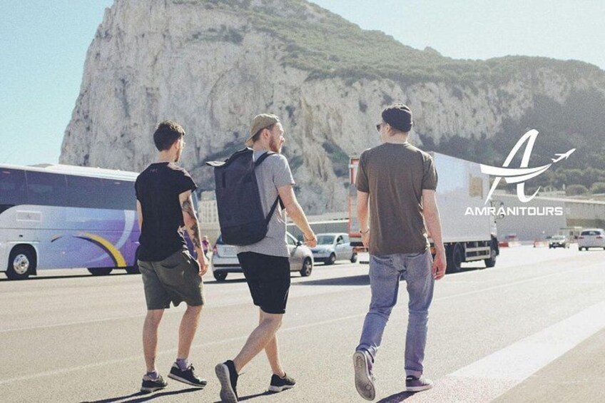 Trois personnes marchent sur une route, avec un autobus et un camion en arrière-plan. 1