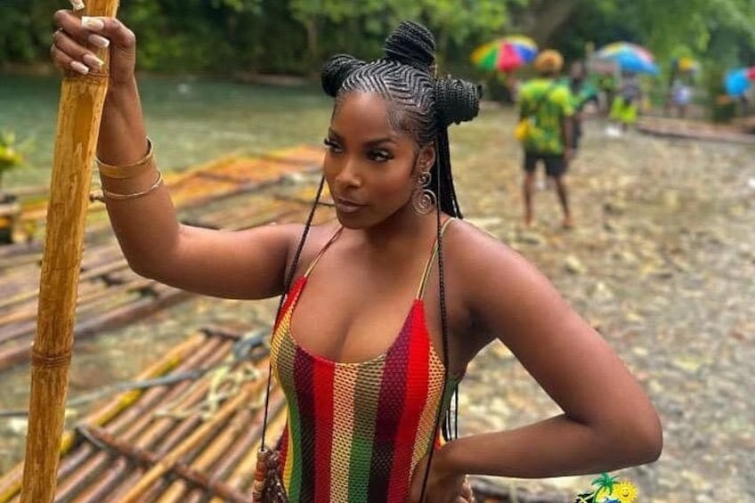 A person in a colorful swimsuit holding a wooden pole, standing on a wooden platform by a body of water. 1