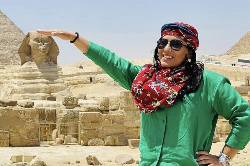 A person in a green shirt and red scarf standing in front of the Sphinx in Egypt. 1