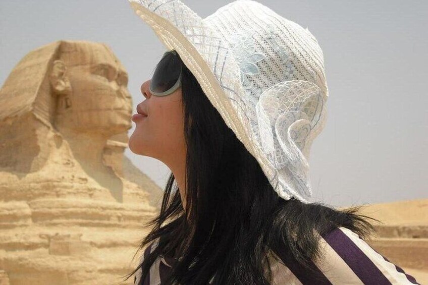 A person wearing a straw hat and striped shirt standing in front of the Great Sphinx of Giza. 4