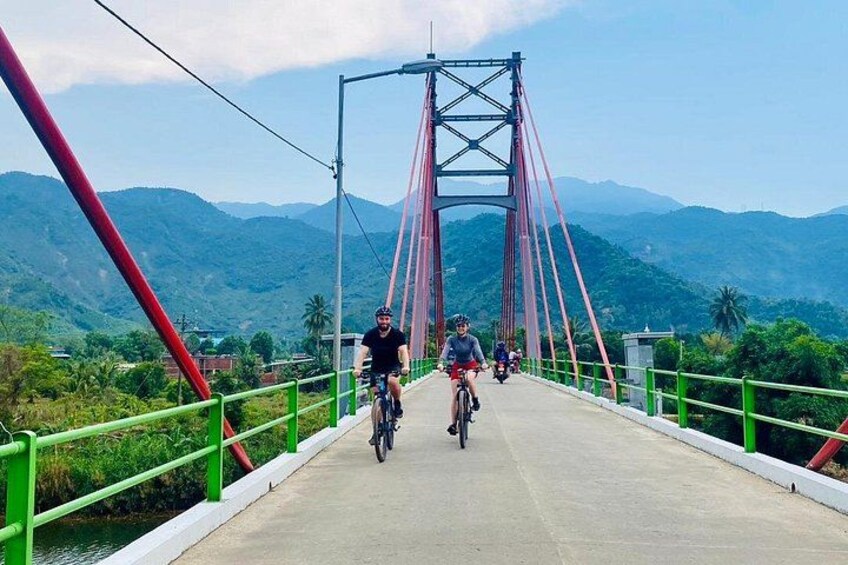 Un pont où l’on voit des cyclistes, des garde-corps verts et, en arrière-plan, un paysage montagneux. 4
