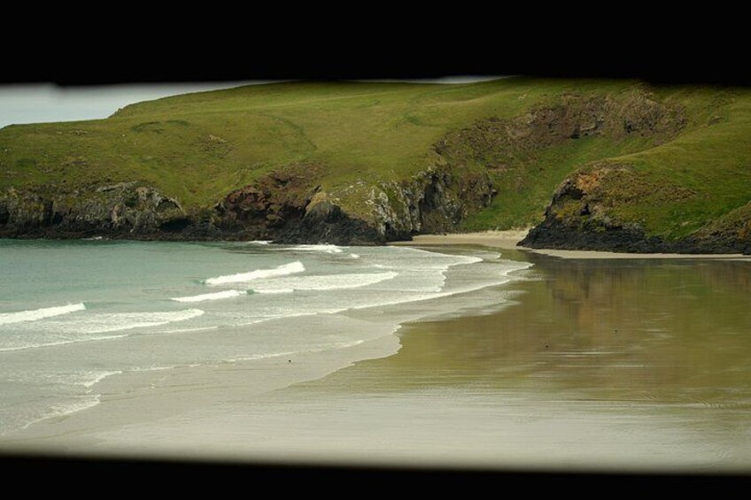 Een strand met golven, groene heuvels en een rotsachtige kustlijn. 3