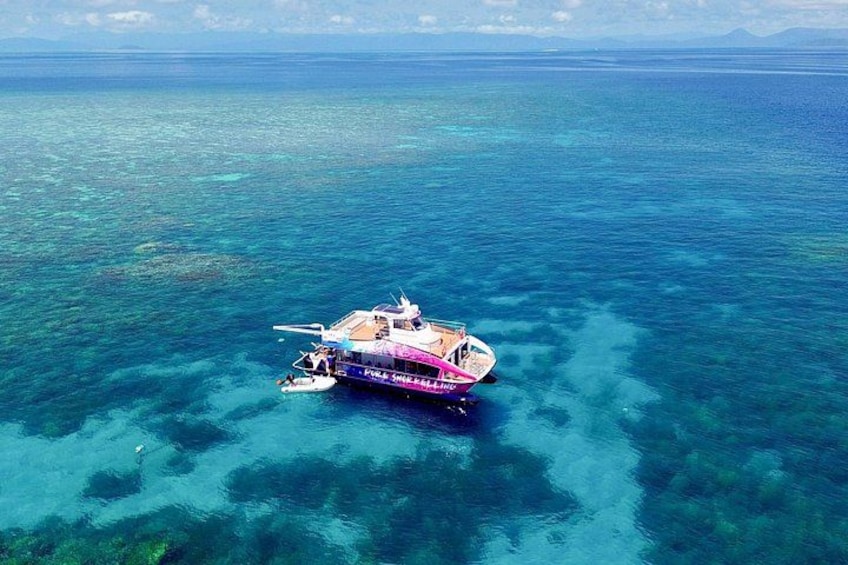 A boat on clear turquoise water with visible coral reefs. 1