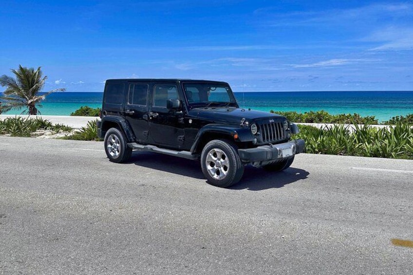 A black SUV parked on a road with a beach and ocean in the background. 3