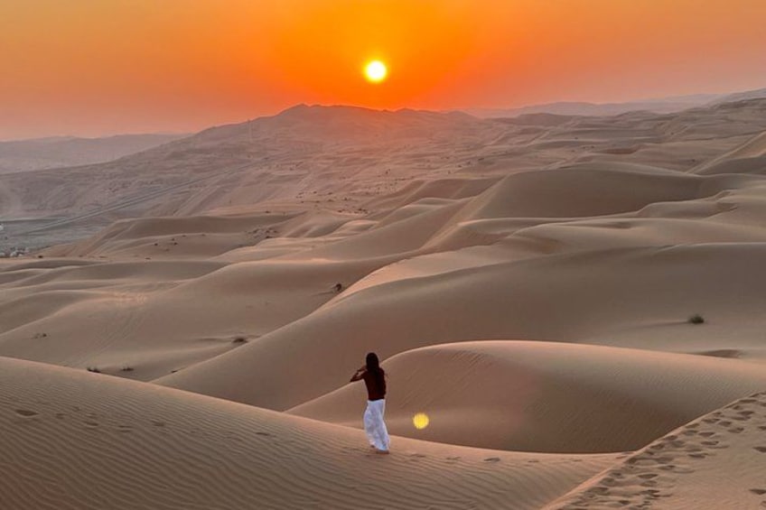 A person walking on sand dunes during sunset. 2