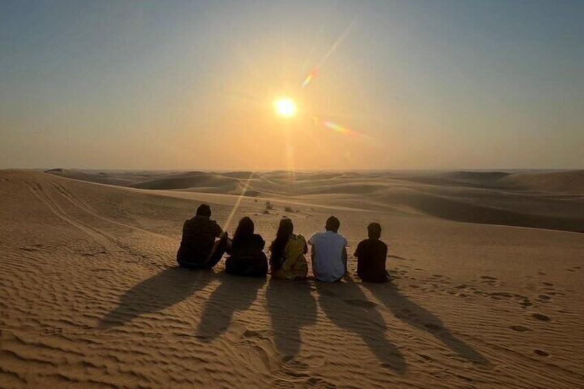 A group of people sitting on a sand dune at sunset. 2
