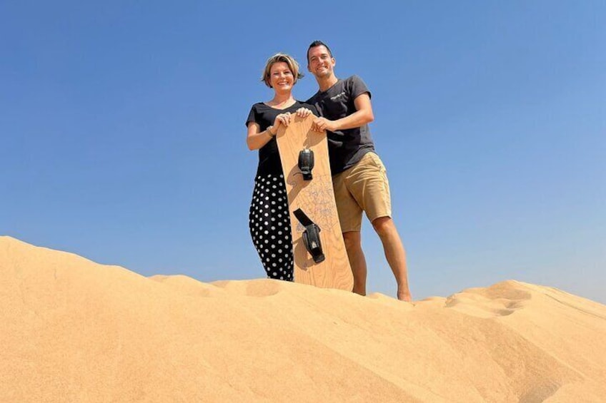 Two people standing on a sand dune with a wooden board. 5