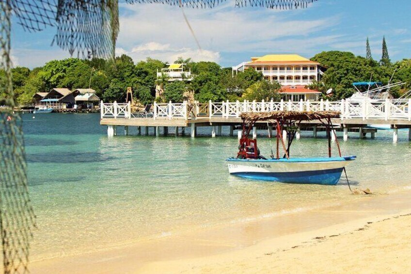 Una spiaggia limpida con un molo di legno, una barca blu e un edificio sullo sfondo. 1