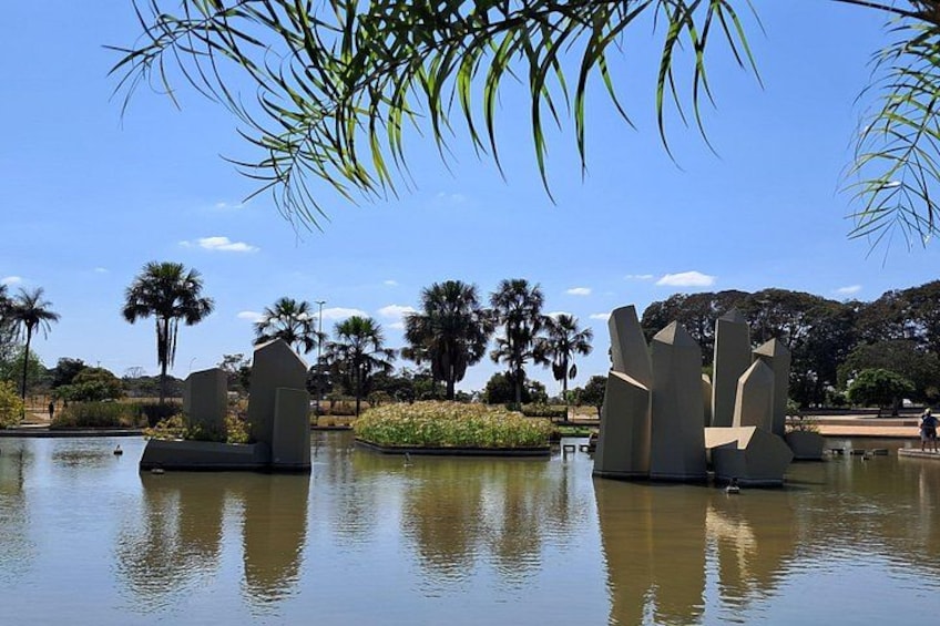 A calm lake with abstract sculptures, palm trees, and a clear blue sky. 4