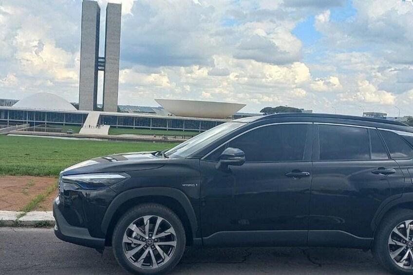 A black SUV parked in front of a modern building with two tall towers. 2