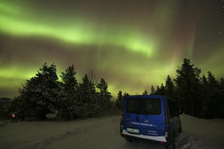 A blue van parked on a snowy road with the Northern Lights in the background. 1