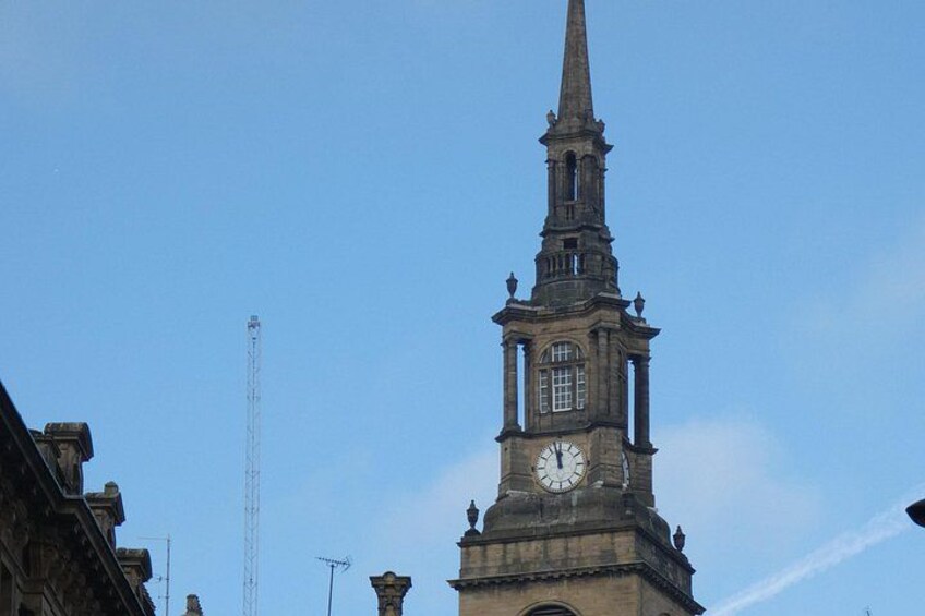 Una torre del reloj con aguja, cielo despejado y una torre de comunicaciones a lo lejos. 4