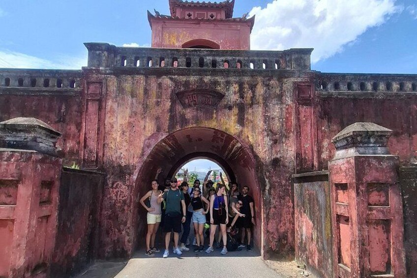 A group of people standing under a large, rusted archway with a traditional roof. 4
