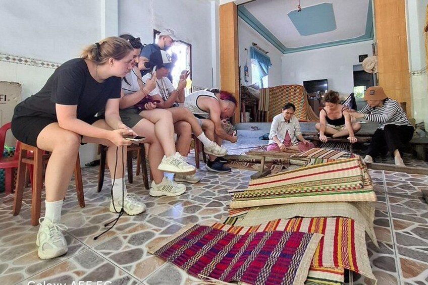 A group of people sitting on chairs, working on colorful woven mats. 2