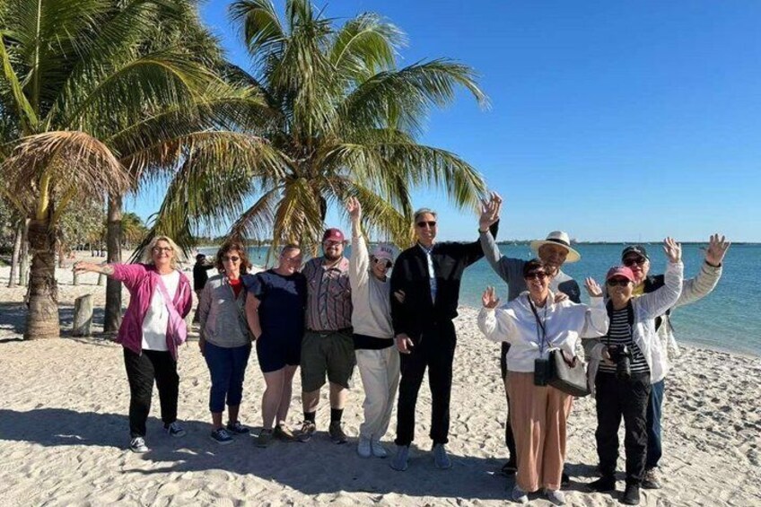 Un grupo de personas en una playa arenosa, con palmeras y el océano al fondo. 1