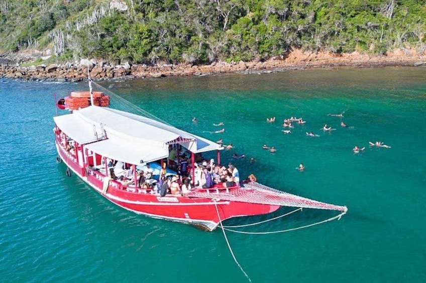 Una barca rossa con persone che nuotano nell'acqua e una costa boscosa sullo sfondo. 2