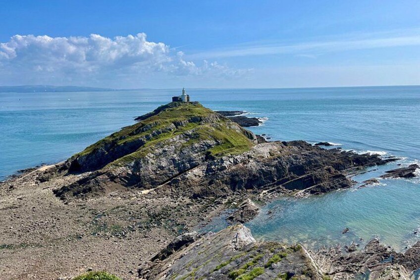 A rocky coastline with a lighthouse on a grassy hill. 4