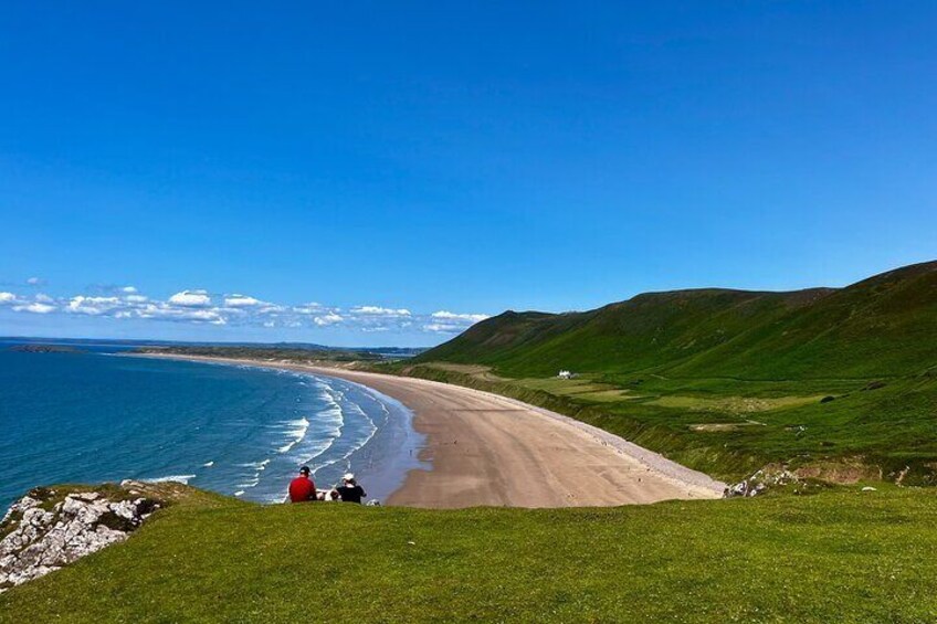 Ett kustlandskap med en strand, grönskande kullar och en klarblå himmel. 3
