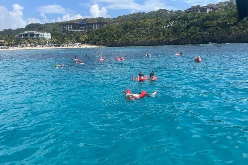 People swimming in a clear blue sea with a beach and buildings in the background. 4