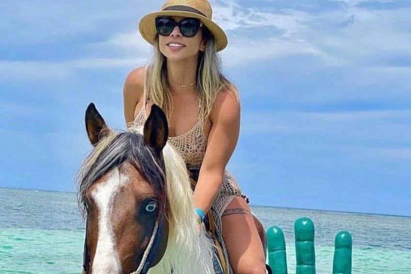 A person riding a horse on a boat with turquoise water and a clear sky in the background. 1