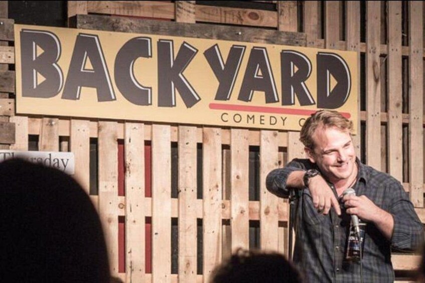 Une personne se tient devant une enseigne sur laquelle on peut lire : « BACKYARD COMEDY CLUB ». 4